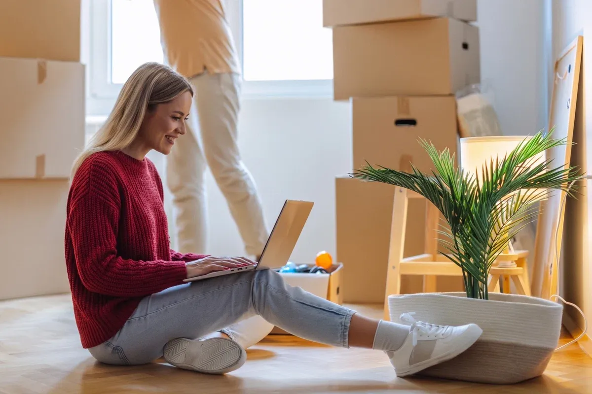 Woman sitting among moving boxes and using a laptop, signifying changing internet when she moves.